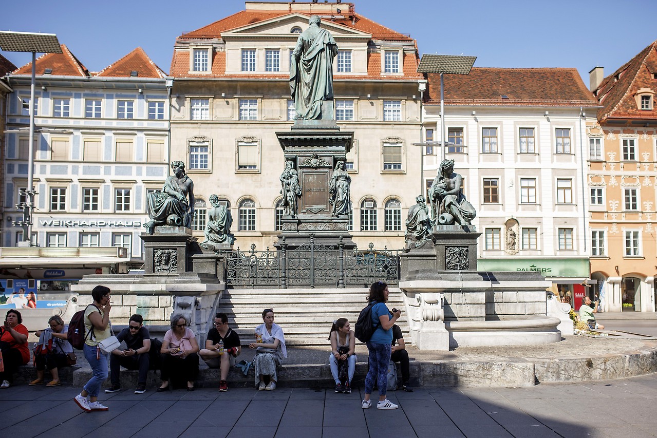 People sit in front of a monument in Graz